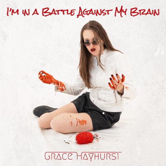 Artwork for 'I'm In A Battle Against My Brain'. Grace Hayhurst is sat on the floor holding a brain covered in blood in an entirely white liminal space.